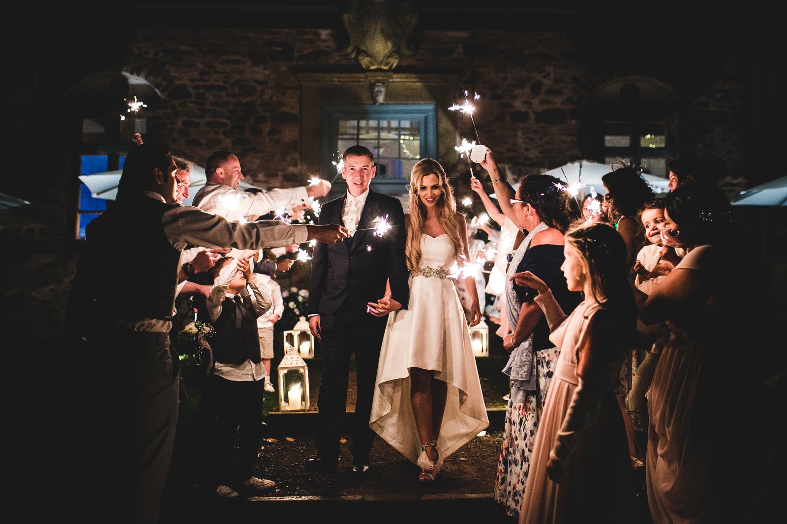 Couple walking out of stone barn hand in hand through sparklers.