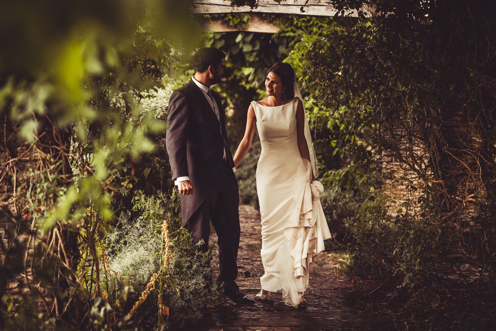 Bride and groom walk hand in hand through the leafy pergola at Hestercombe Gardens wedding