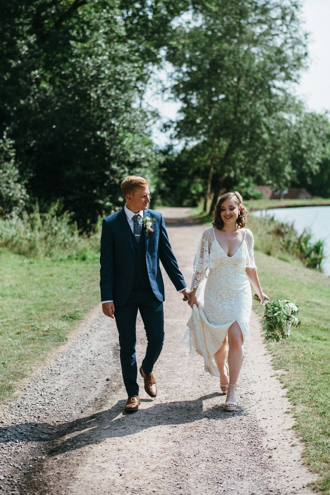 Bride and groom wander in a relaxed manner alongside the lake, hand in hand